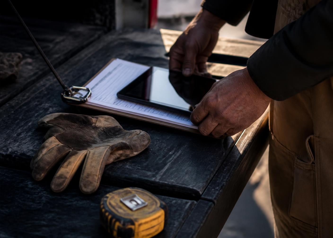 A contractor filling out an estimate on a clipboard and tablet at a truck tailgate